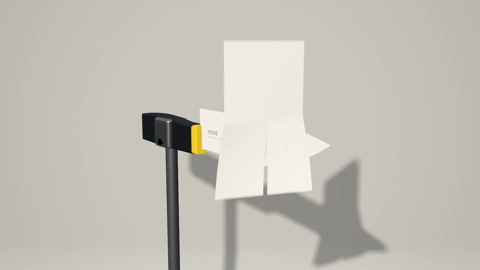 A white zirconia chef’s knife held edge up in a grey test clamp; a sheet of paper falls onto the edge and parts in two halves, in slow motion, against a grey studio wall.